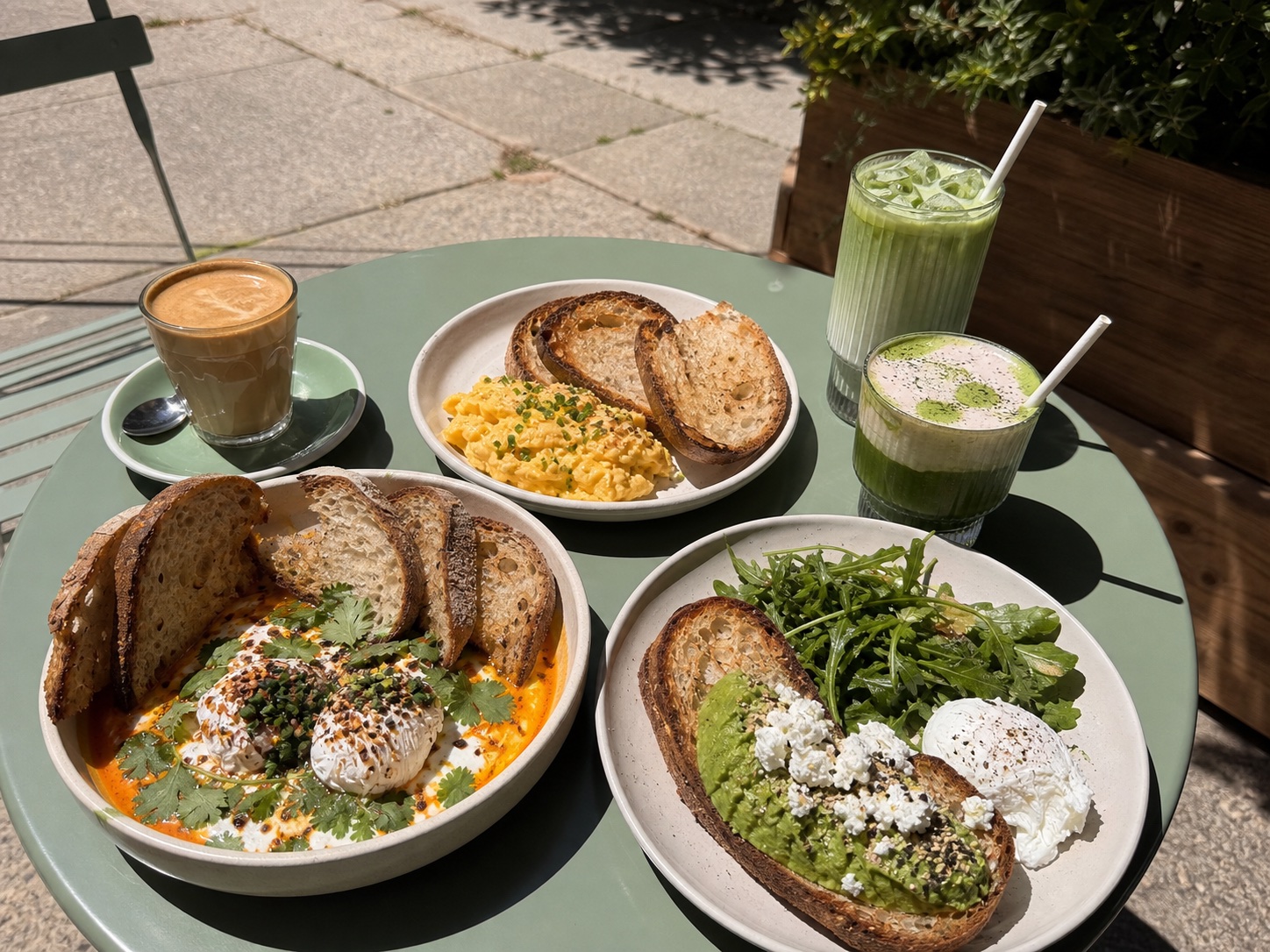 Brunch plates, coffee and matcha on a green outdoor table